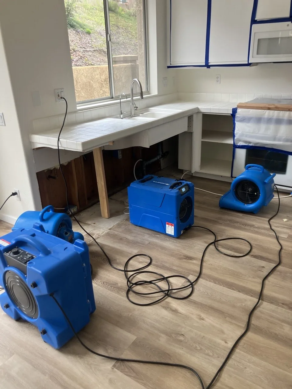 Kitchen with an air scrubber, dehumidifier and air mover running, cabinets wrapped in plastic