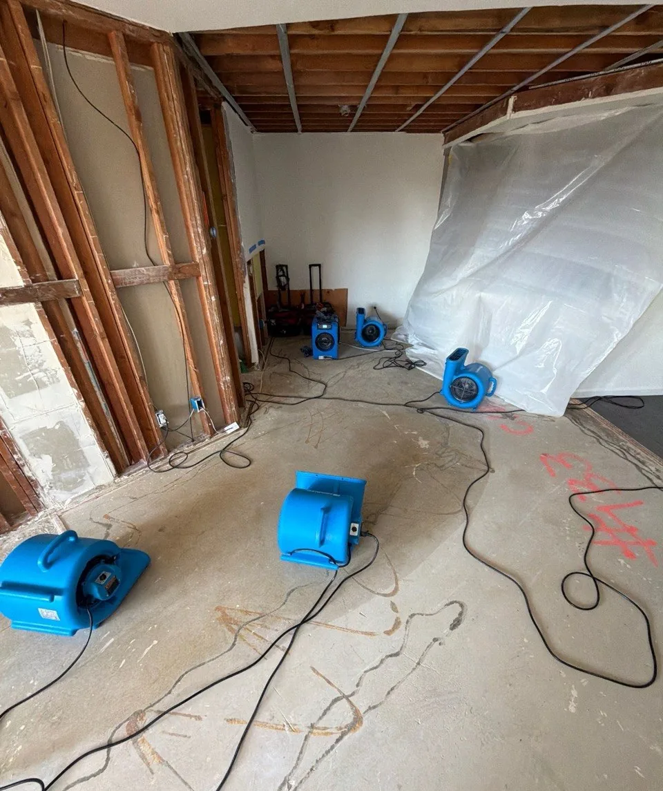Condo living room with wet drywall and ceiling removed, air movers and plastic containment