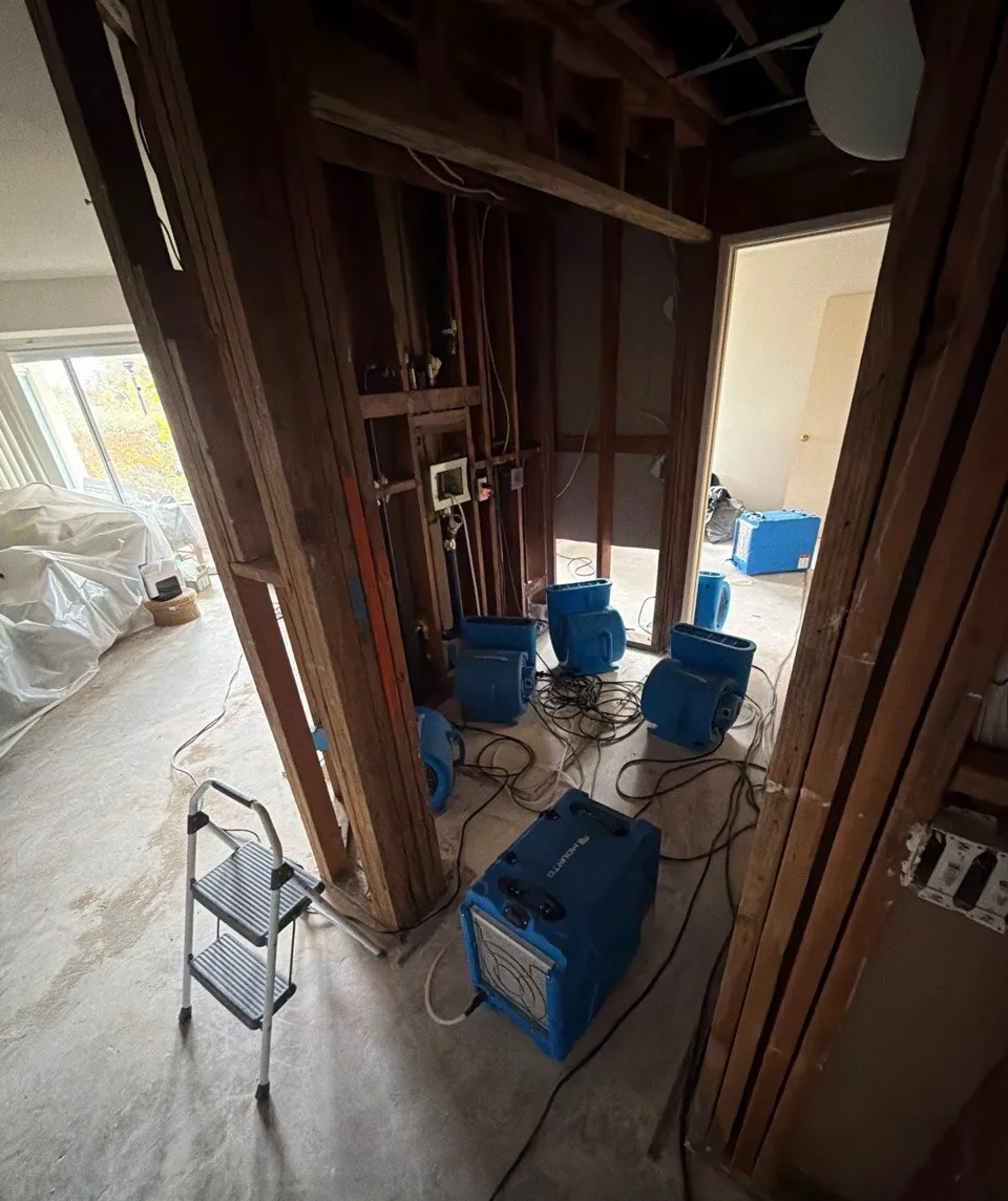 Hallway with open wall framing, air movers and a dehumidifier drying the structure