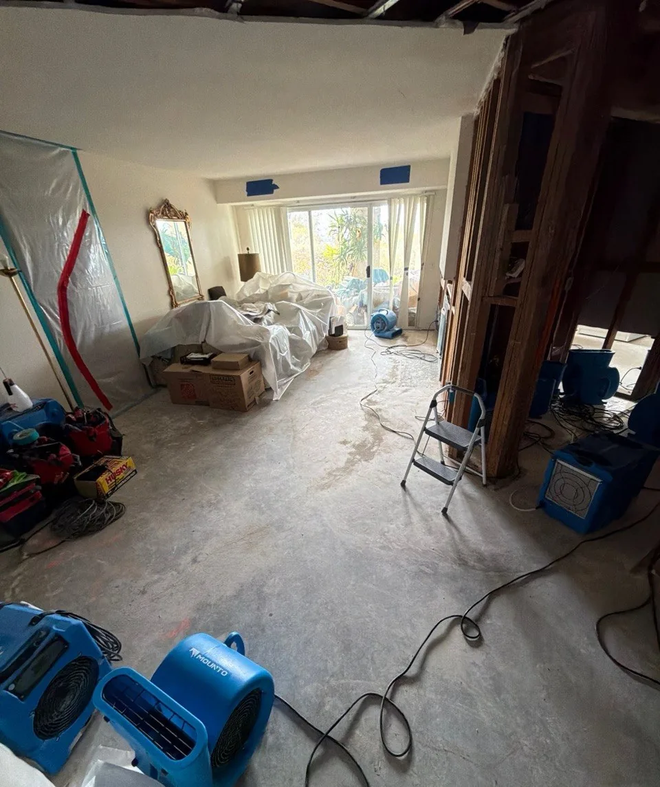 Living room furniture covered in plastic next to a zippered containment wall